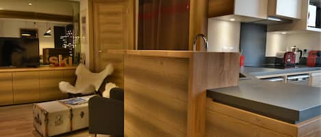 A modern kitchen with wooden cabinetry, a built-in island, and a seating area with a white fur chair.