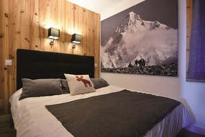 A bedroom with a wooden wall panel, a bed with a white and gray duvet, two wall-mounted lights, and a mountain landscape painting. - Chalet-style accommodations at the base of the slopes, Méribel Mottaret (Méribel-Mottaret)