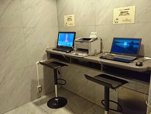 Un espacio de trabajo con dos computadoras portátiles, una impresora y una tableta sobre una encimera de baldosas de mármol.