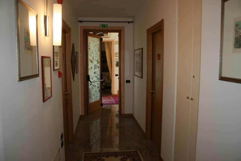 Un corridoio con quadri appesi alle pareti, un pavimento rivestito di moquette e una porta in fondo che dà su un'altra stanza.