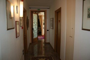 Un pasillo con cuadros enmarcados en las paredes, piso alfombrado y una puerta al final que da a otra habitación.