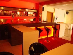 Una zona de bar con mostrador, taburetes y alfombra roja.