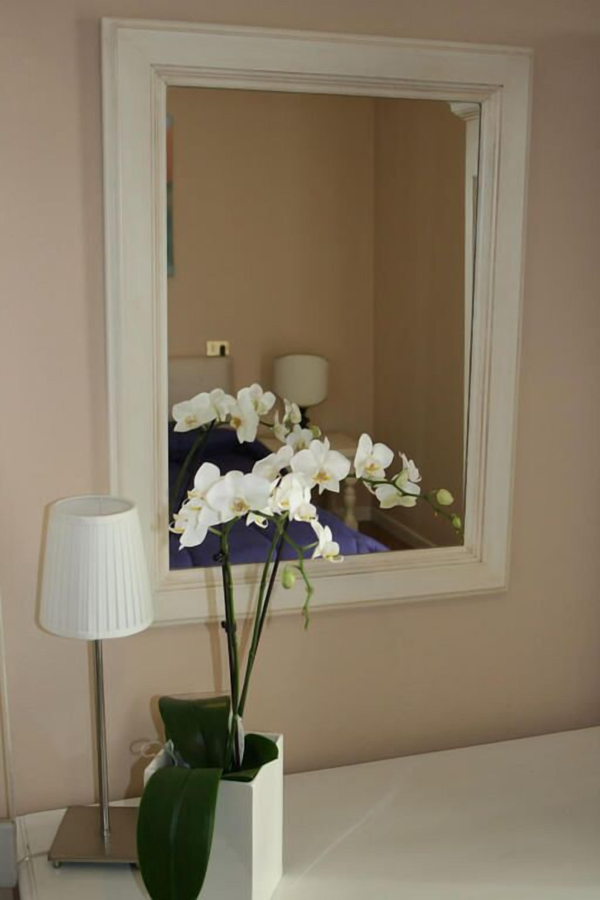 A bathroom with a large mirror, a potted orchid, and a lamp.