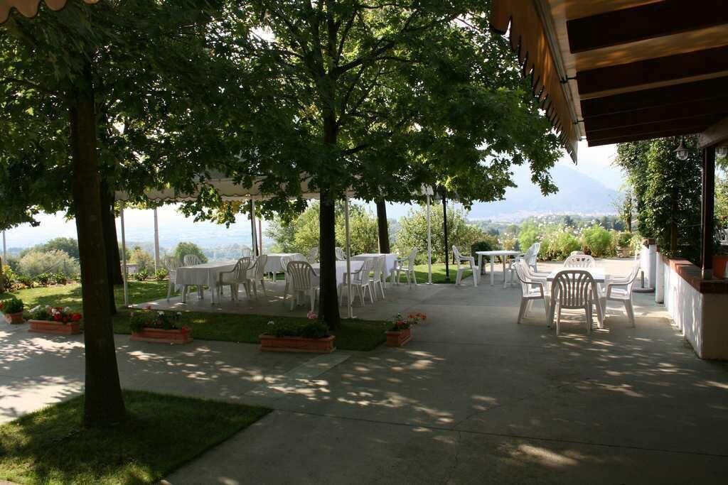 An outdoor patio area with white plastic tables and chairs, surrounded by trees and a view of a mountainous landscape.