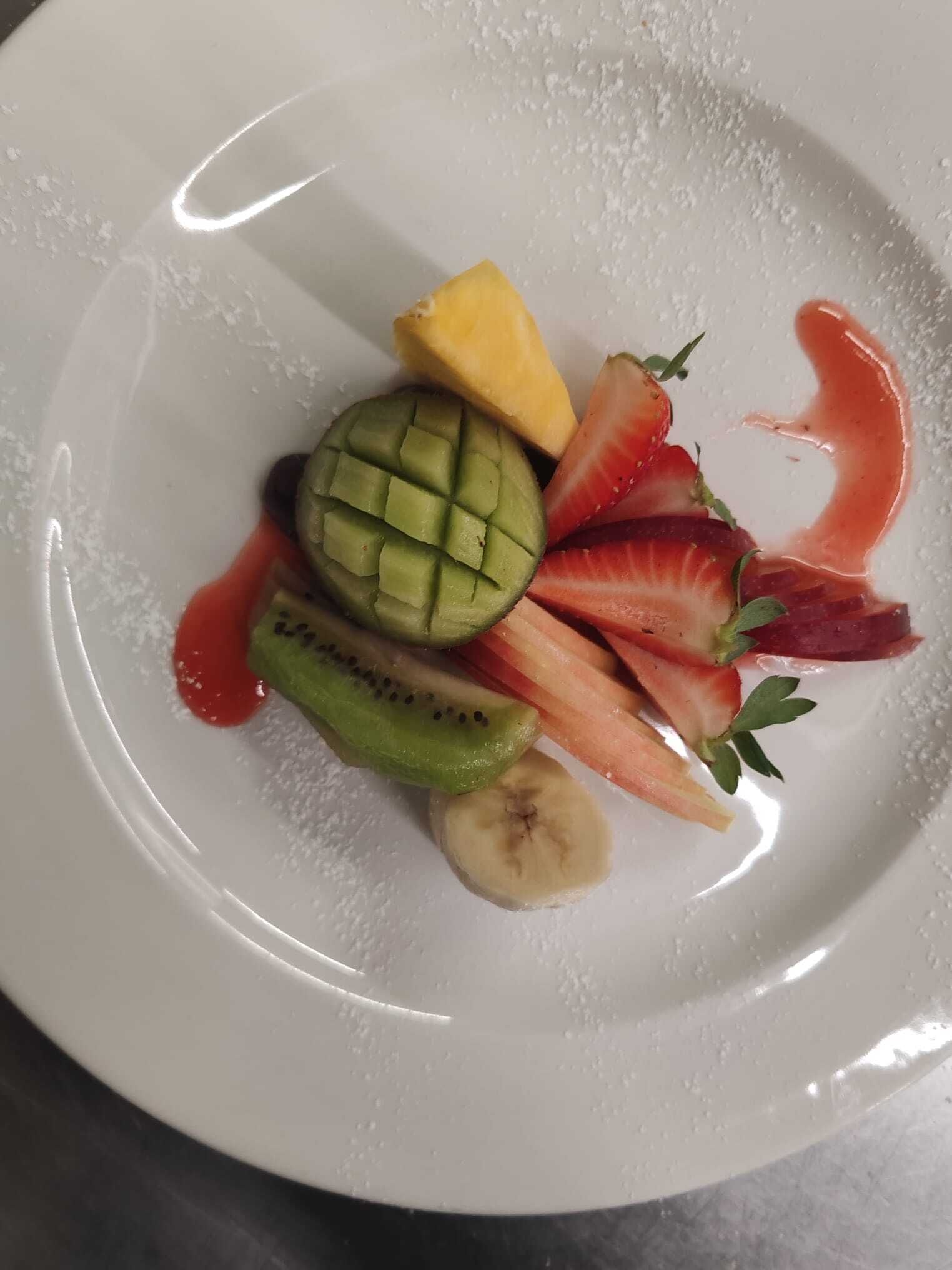 Un plato blanco con varias frutas, incluyendo kiwi, plátano, fresa y mango.