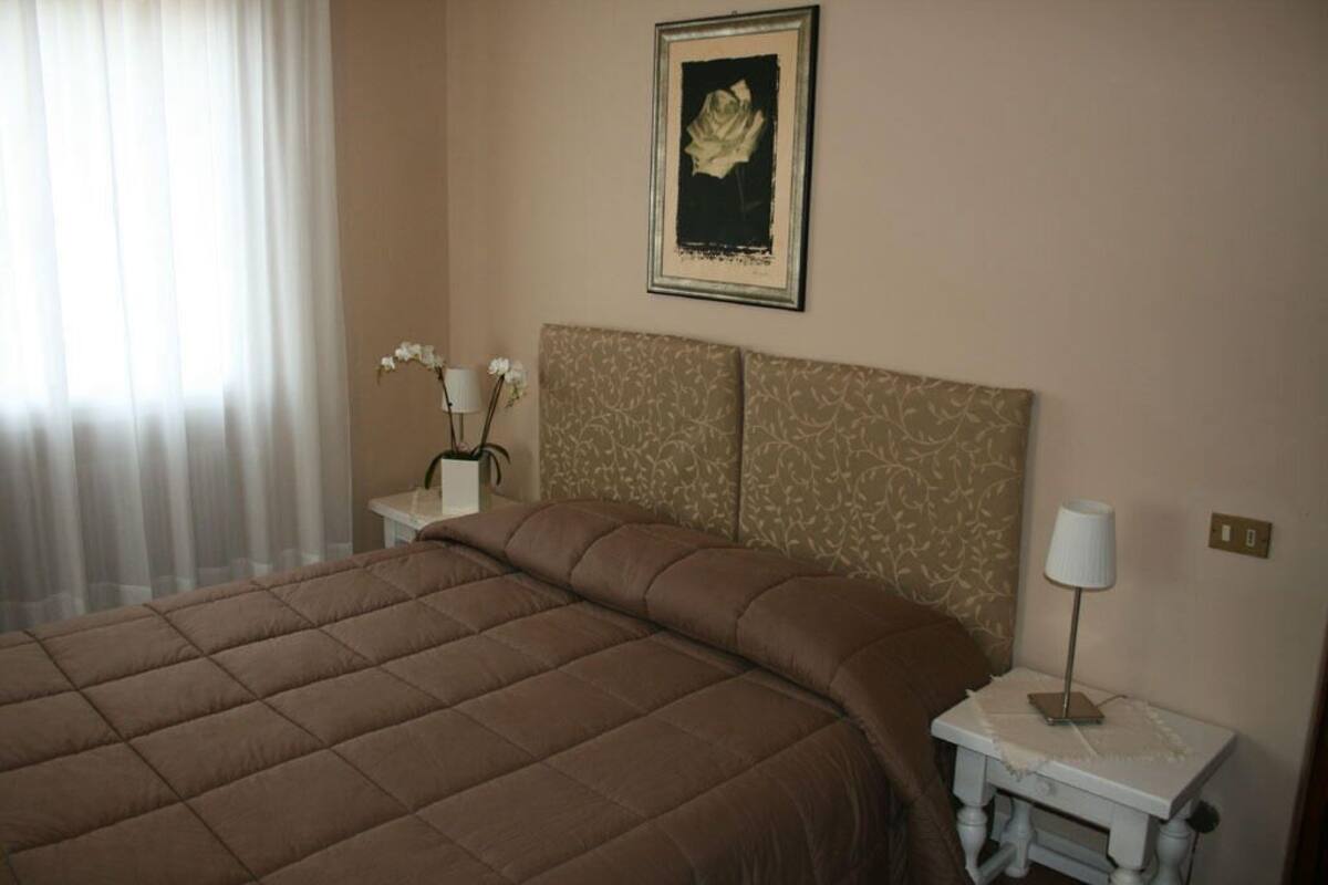 A neatly made bed with a brown bedspread, a bedside table with a lamp, and a framed picture on the wall.