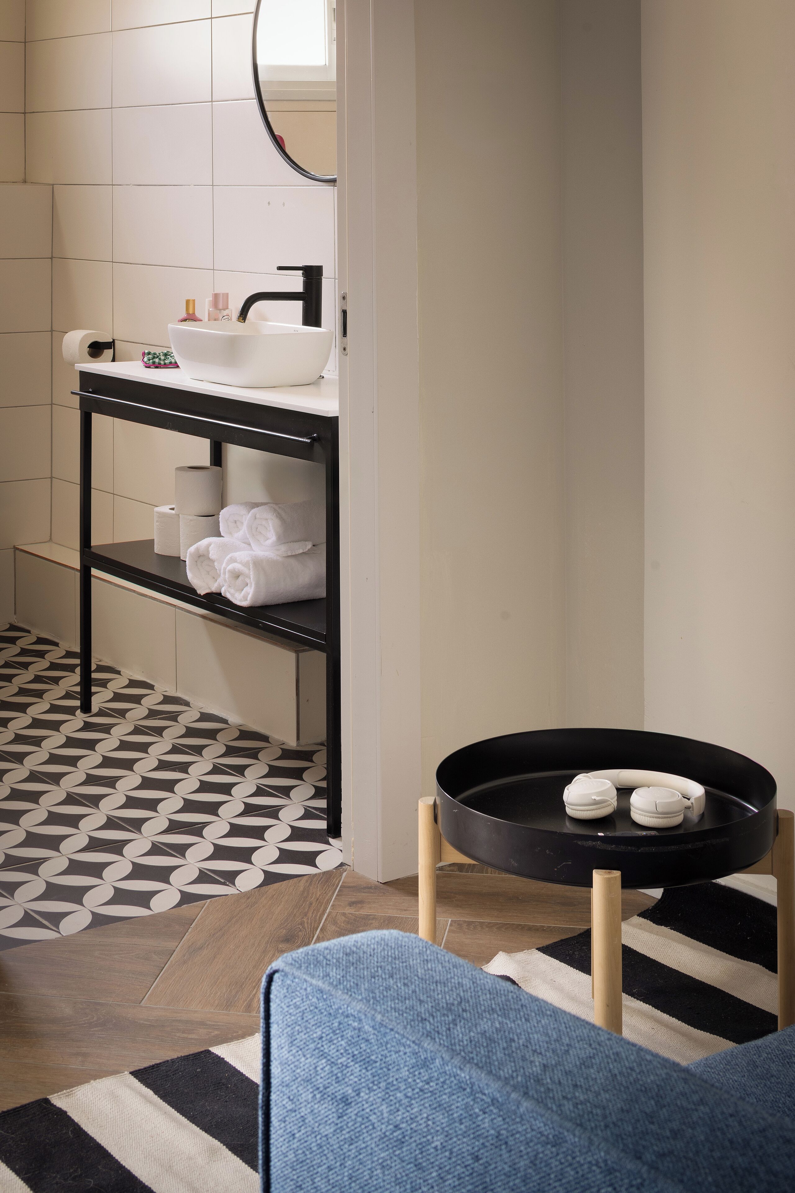 A bathroom with a white sink, black shelf, and a black tray with towels.
