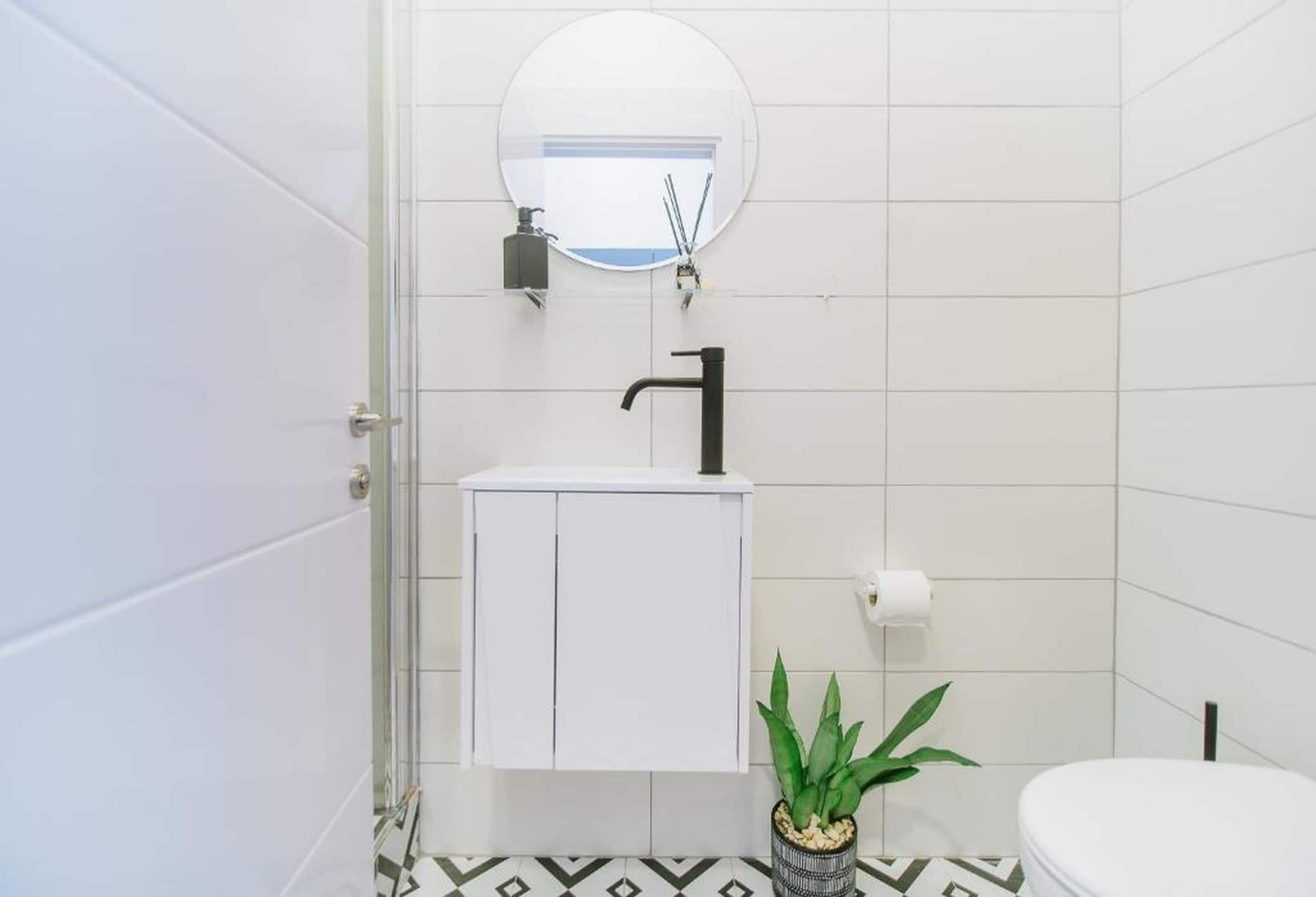 Un baño con lavamanos blanco, espejo, inodoro y planta en maceta.