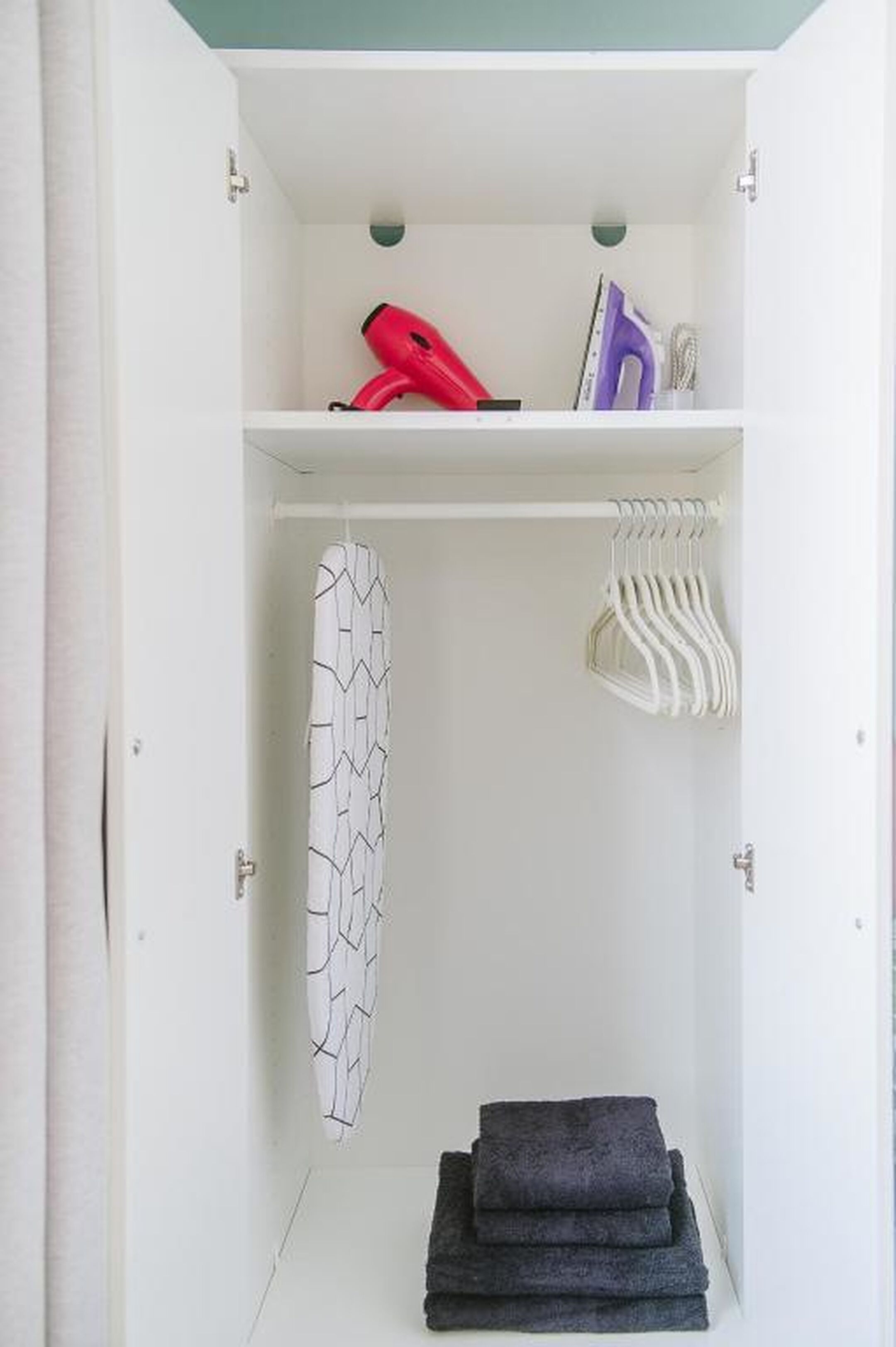 A wardrobe with a hanging iron, a steamer, and neatly folded towels.