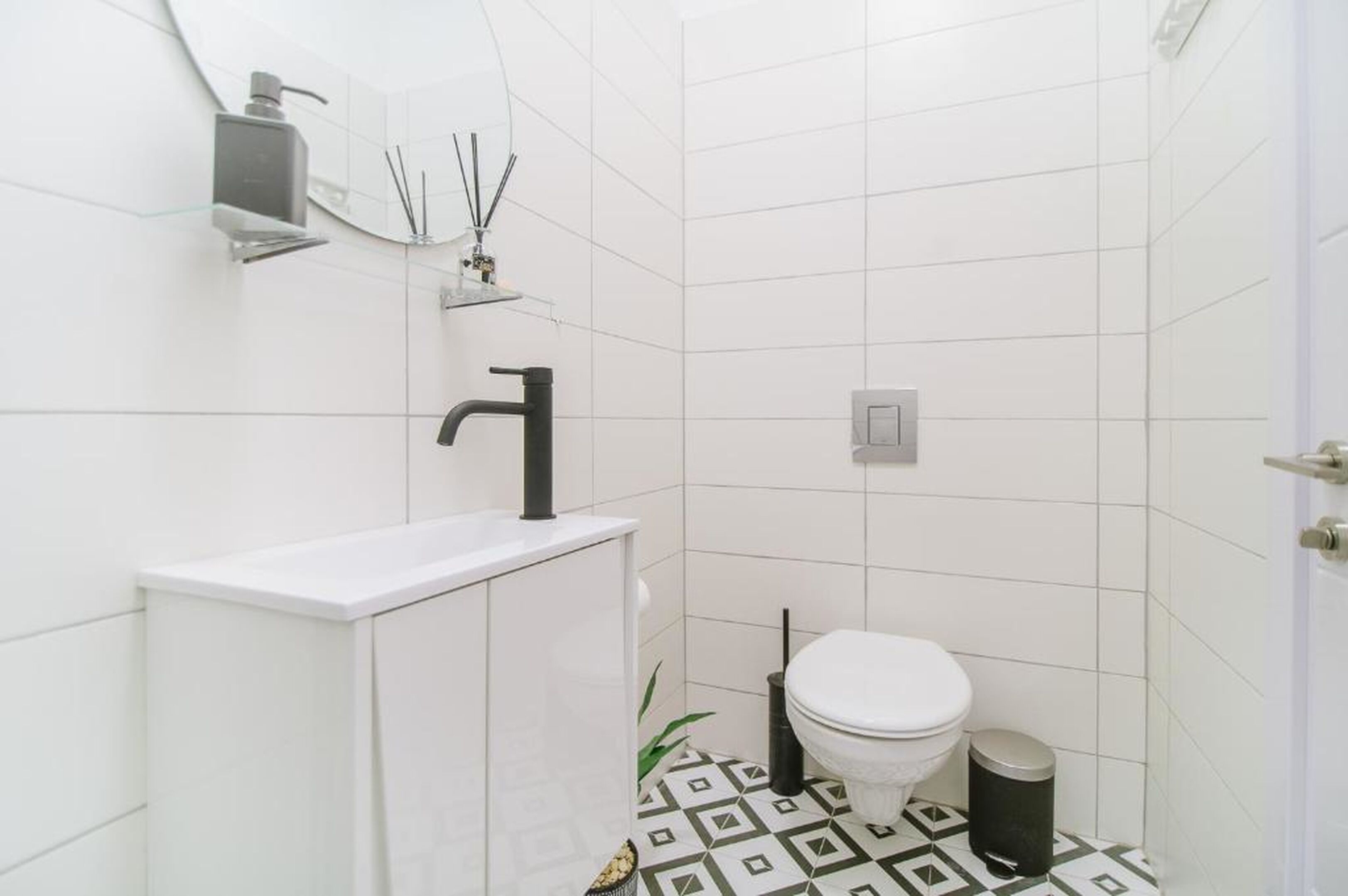 A small bathroom with a white sink, black faucet, white toilet, and a trash bin.