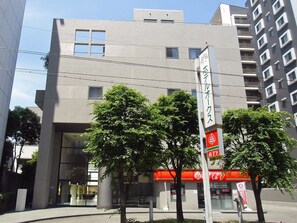 Un bâtiment moderne doté d’une grande entrée en verre, entouré d’arbres et d’une enseigne rouge et blanche indiquant un commerce.