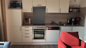 Eine kleine Küche mit Mikrowelle, Backofen, Geschirrspüler und einem roten Sofa.