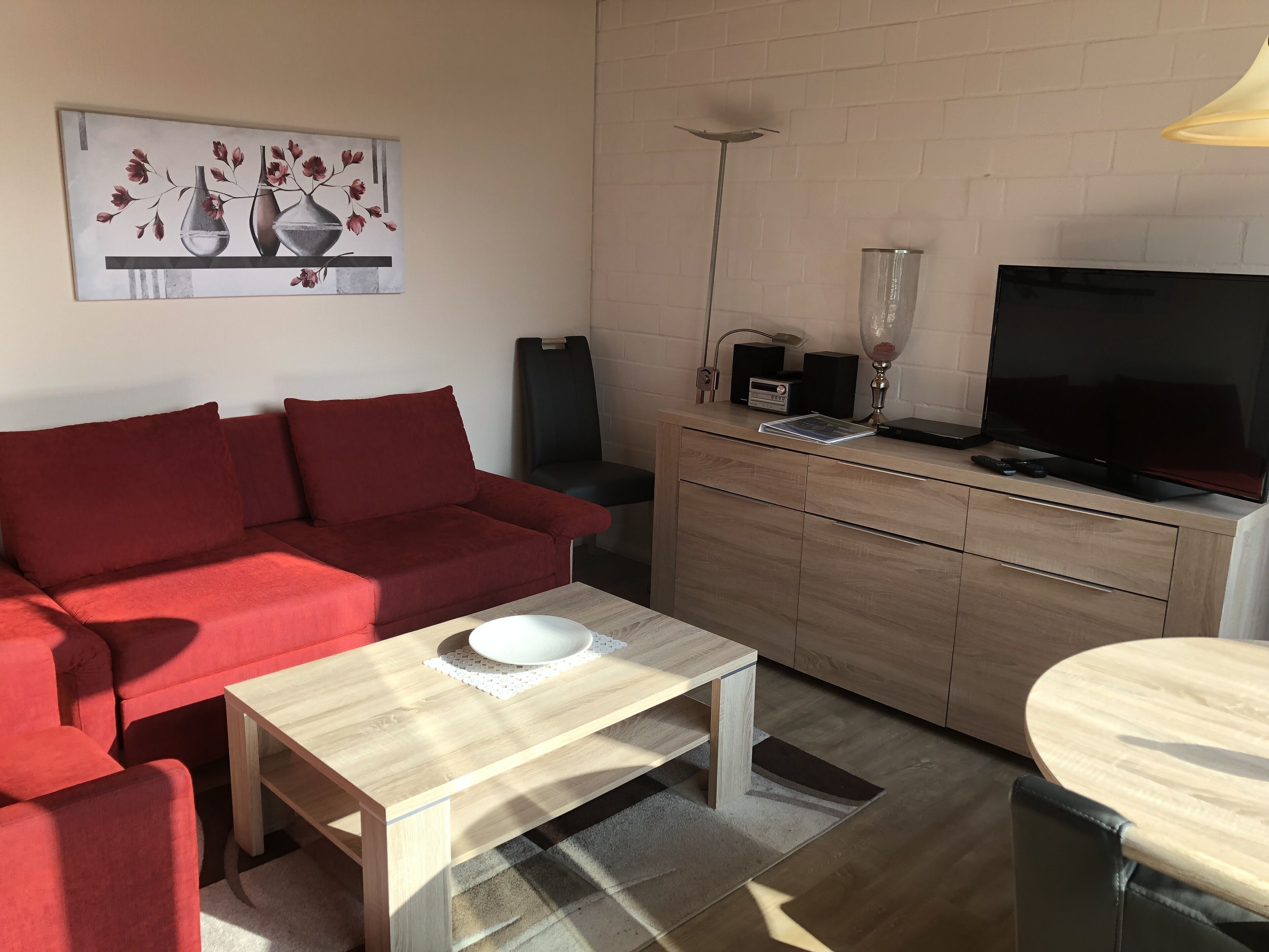 A modern living room with a red sofa, a wooden coffee table, a TV, and a painting on the wall.