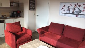 Ein kompakter Wohnbereich mit Küchenzeile, einem roten Sofa und einem Couchtisch.
