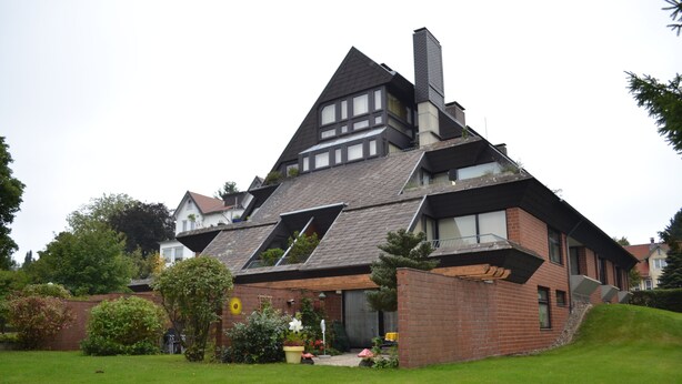 Ein modernes Haus mit geneigtem Dach, einer Ziegelaußenwand und einem kleinen Garten.