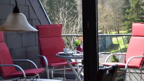 Ein Balkon mit roten Stühlen und einem Tisch, einer Hängelampe und Blick auf Bäume und eine Rasenfläche.