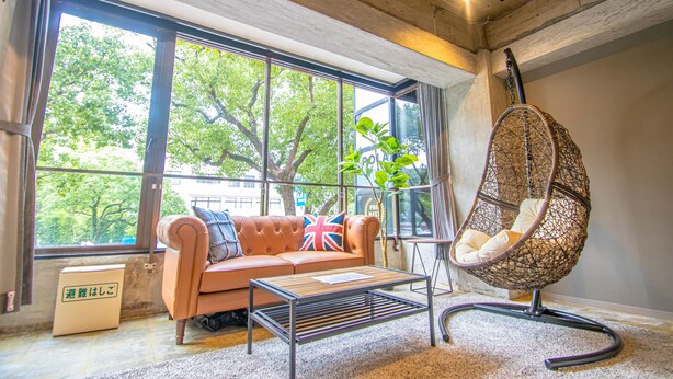A modern living room with a sofa, a hanging chair, and large windows offering a view of trees. - AMP FLAT Nishijin 2F (Fukuoka)