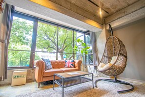 Una sala moderna con un sofá, una silla colgante y ventanas amplias con vistas a árboles.