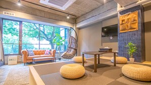 A modern interior with a sofa, round ottomans, a table, and a TV mounted on the wall. - AMP FLAT Nishijin 2F (Fukuoka)