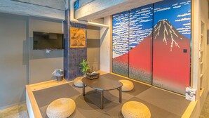 A meeting room with a table, four round seating areas, a television, and a wall with a mountain painting. - AMP FLAT Nishijin 2F (Fukuoka)