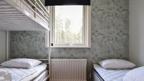 A dormitory room with bunk beds, a window with a view of trees, and patterned wallpaper.
