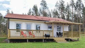 A single-story cabin with a red-tiled roof, a covered porch with a railing, and a grill on the deck.