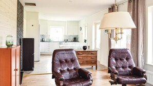 A spacious living room with two leather armchairs, a wooden cabinet, and a large window with a hanging lamp.