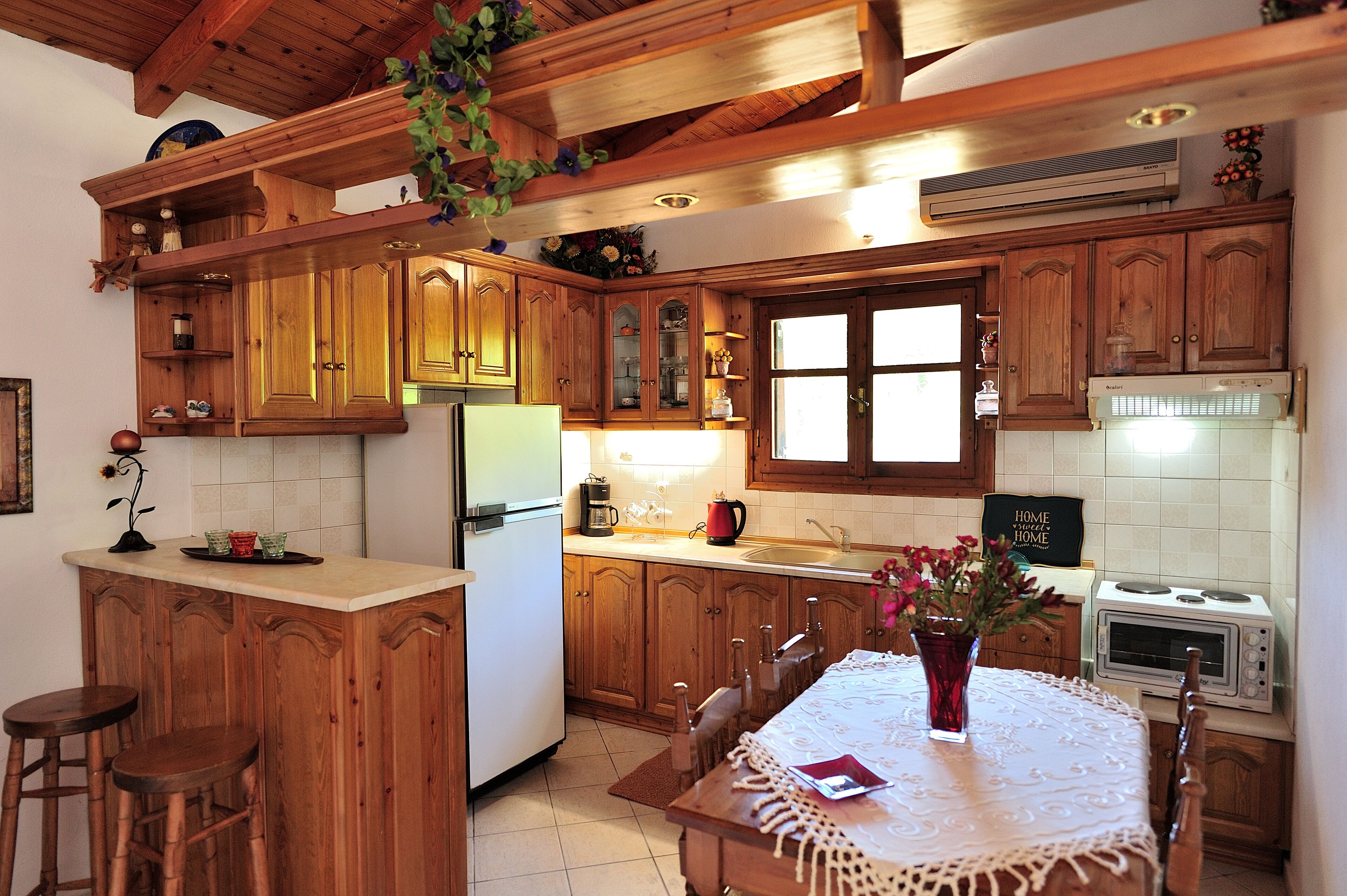 A kitchen with wooden cabinets, a central island with stools, a dining table with a vase, and a sign that reads "HOME VENTURES".