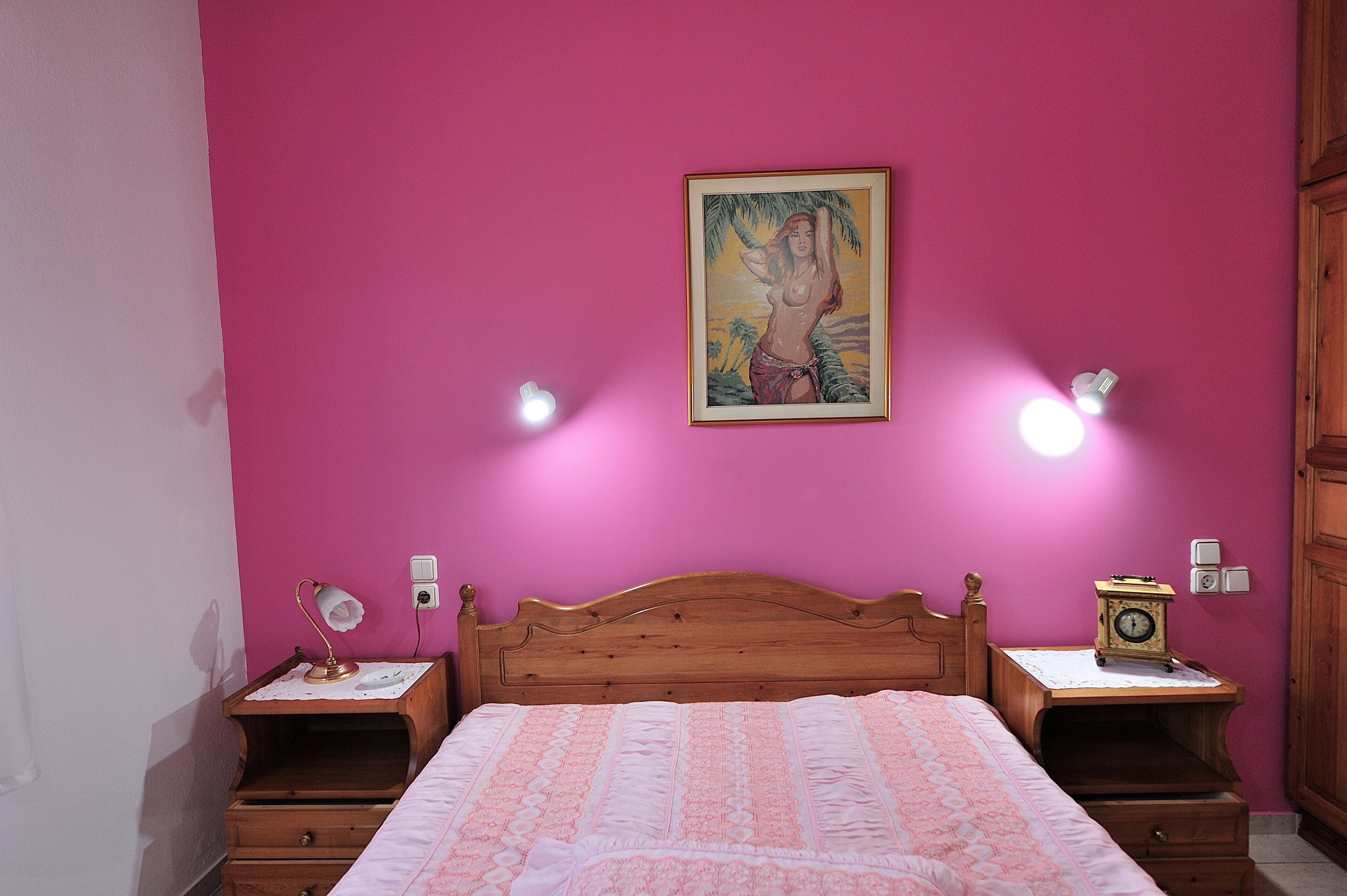 Ein Schlafzimmer mit einem hölzernen Bett, rosafarbenen Wänden, zwei Nachttischen mit Lampen und einem Bild an der Wand.