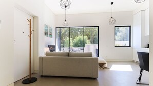 A modern living room with a sofa, a coat rack, and a dining area with a table and chairs.