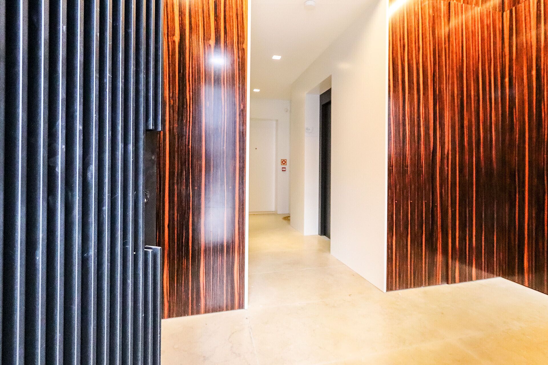 A modern hallway with a glossy wooden floor and walls, leading to a door with a black metal handle.