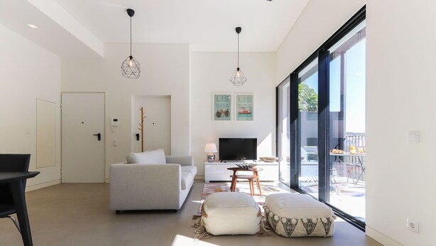 A modern living room with a sofa, ottoman, TV, and a dining area with a table and chairs.
