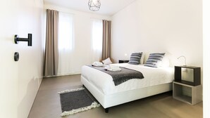 A modern bedroom with a bed, bedside tables, a hanging light fixture, and a view of the outside through large windows.