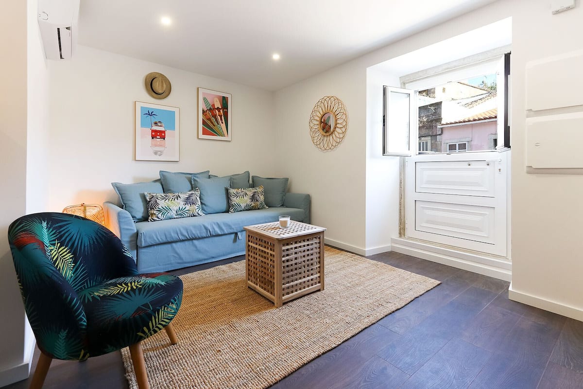 A living room with a blue sofa, a patterned armchair, a small wooden table, and a woven rug.