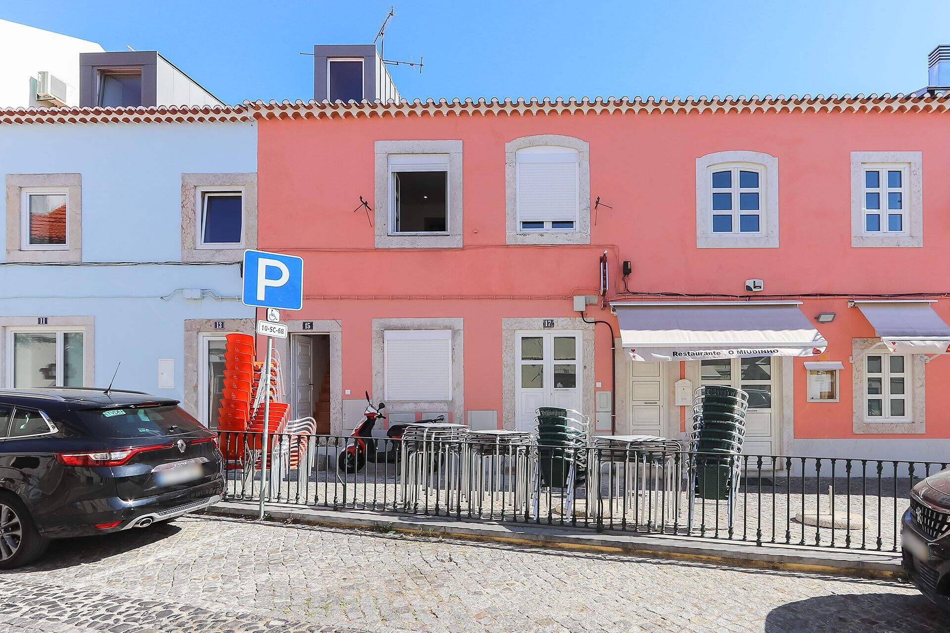 A street with a row of colorful buildings, a parking sign, and a car parked on the side.