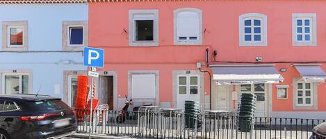 A street with a row of colorful buildings, a parking sign, and a car parked on the side.