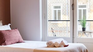 Ein Hotelzimmer mit Bett, einem Fenster mit Blick auf Gebäude und einer Topfpflanze auf dem Balkon.