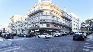 Ein mehrstöckiges Gebäude mit Balkonen, parkenden Autos und einer Kopfsteinpflasterstraße.
