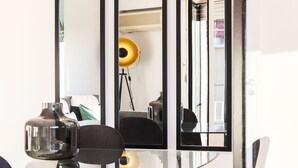 Ein modernes Zimmer mit einem Glastisch, einem Stuhl und einem Spiegel, der eine gelbe Lampe und eine Tür reflektiert.