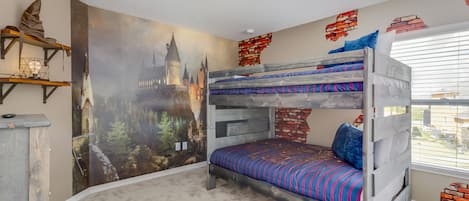 A bunk bed room with a castle mural, brick wall accents, and a window with blinds.