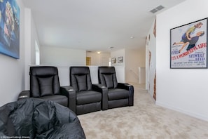 A home theater room with three black leather recliners, a large poster on the wall, and a carpeted floor.