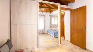 A bedroom with a wooden wardrobe, a bed with a blue cover, and a wooden door. - Armamento Villa (Skiathos)