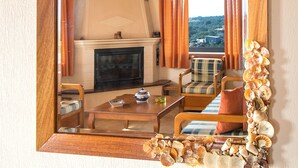 A mirror with a wooden frame decorated with seashells, reflecting a room with a fireplace, a dining table, and a view of the outdoors. - Armamento Villa (Skiathos)