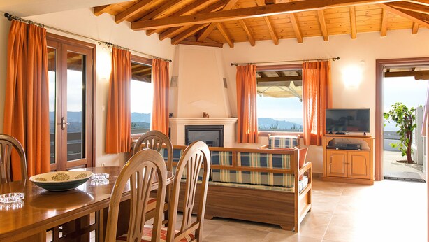 A living room with a fireplace, a television, and a dining area with chairs and a table. - Armamento Villa (Skiathos)