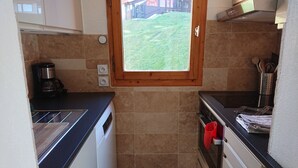 A compact kitchen with a window, a coffee maker, and a red pot hanging on the oven door.