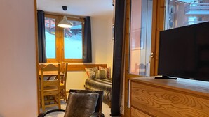 A cozy room with a wooden chair, a sofa, a television on a wooden cabinet, and a window with curtains.