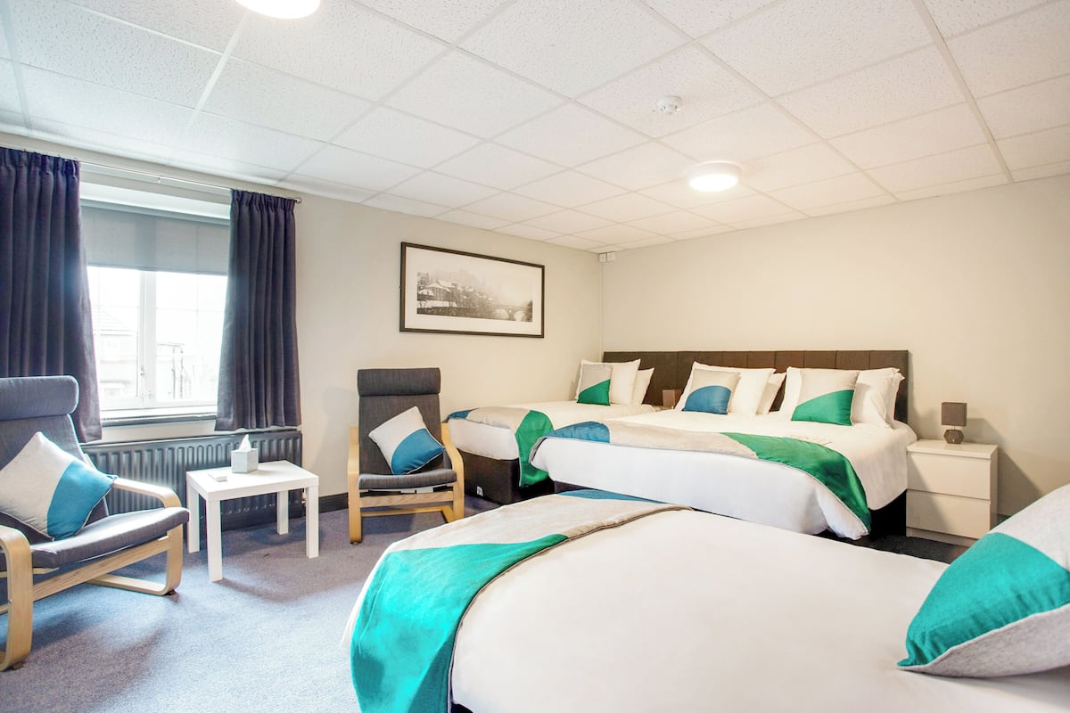 A hotel room with two beds, a chair, a small table, and a nightstand.