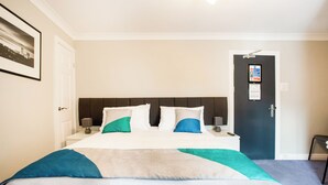 A hotel room with a bed, bedside tables, a nightstand, a door, and a framed picture on the wall.