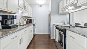 A narrow kitchen with white cabinets, a coffee maker, a toaster, and a refrigerator. - Las Palmas: Spacious 4BR, 2BA home in Holden Beach, ideal for family getaways. (Holden Beach)