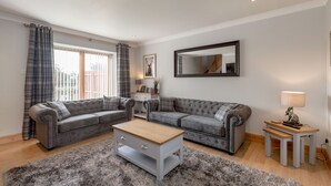 A living room with two grey sofas, a wooden coffee table, a grey shag rug, a small white side table, and a mirror on the wall.